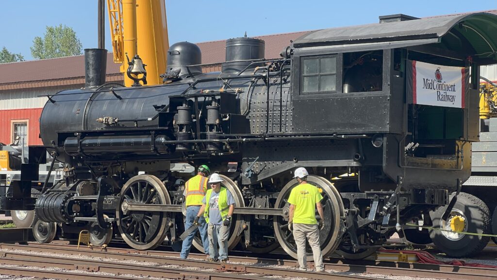 Side view of steam locomotive #1385 sitting on tracks with workers in yellow vests near its wheels.