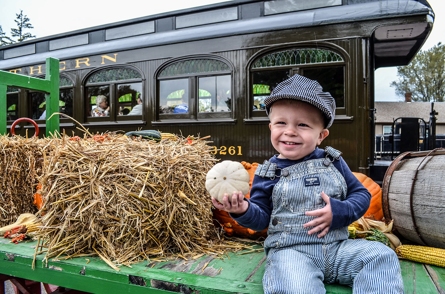 Child in engineer uniform holding gourd next to railroad passenger car