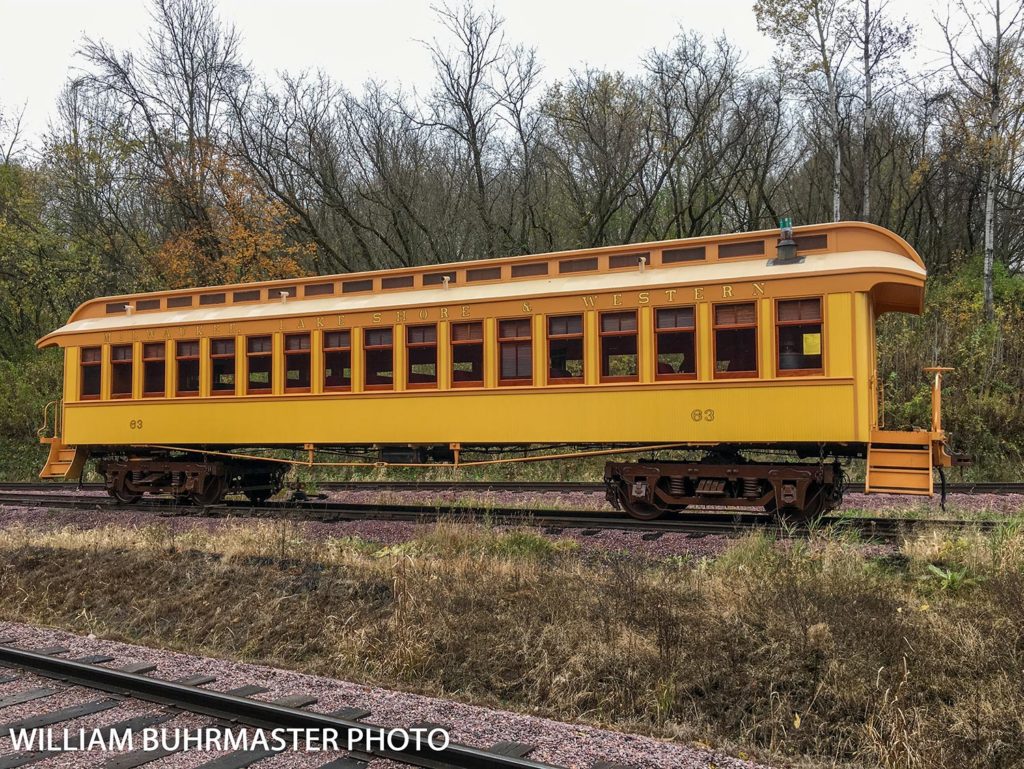 yellow and orange antique railroad passenger car with gold lettering that says Milwaukee Lake Shore & Western above windows and the number 63 near either end of the car